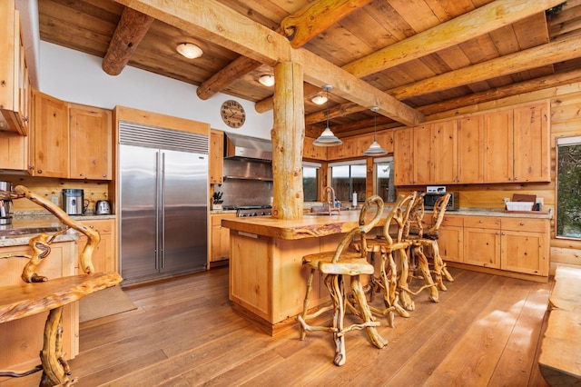 kitchen with wall chimney exhaust hood, sink, built in fridge, and wooden ceiling