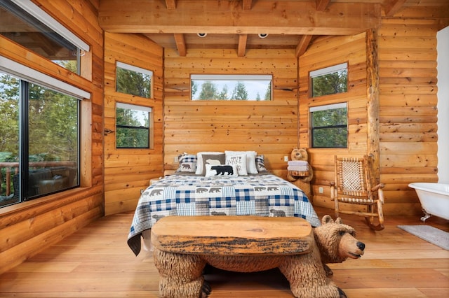 bedroom with multiple windows, a high ceiling, beam ceiling, and light hardwood / wood-style flooring