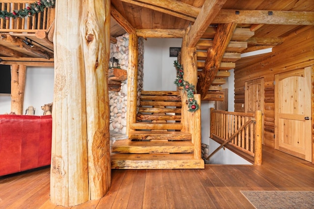 stairs with beam ceiling, hardwood / wood-style floors, log walls, and wooden ceiling