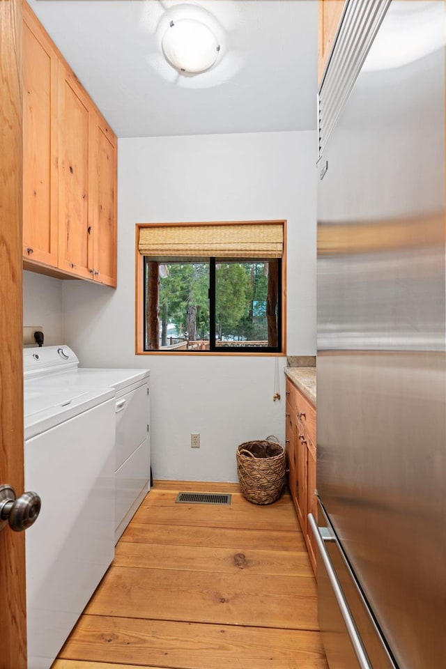 clothes washing area featuring cabinets, washer and clothes dryer, and light hardwood / wood-style floors