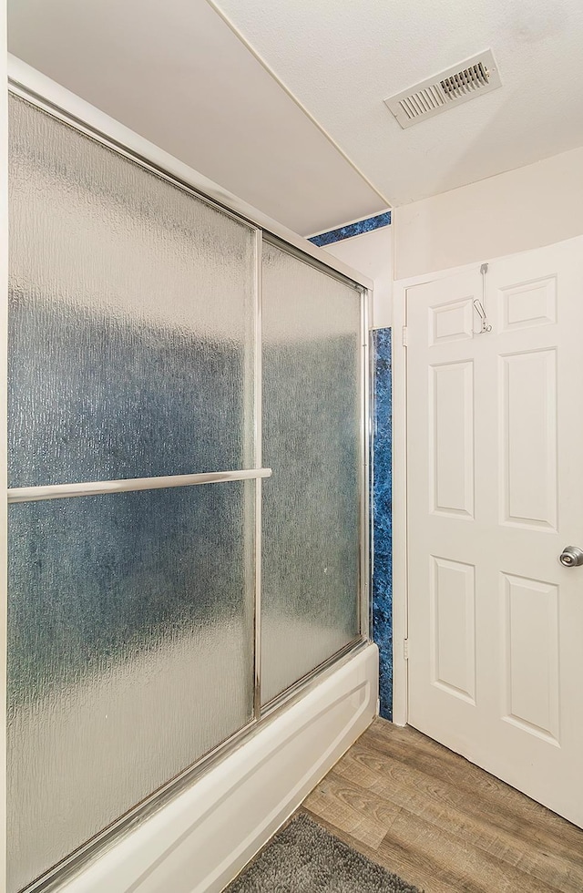 bathroom with hardwood / wood-style flooring and combined bath / shower with glass door