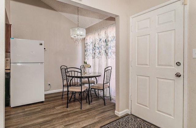 dining room with an inviting chandelier, dark wood-type flooring, a textured ceiling, and vaulted ceiling