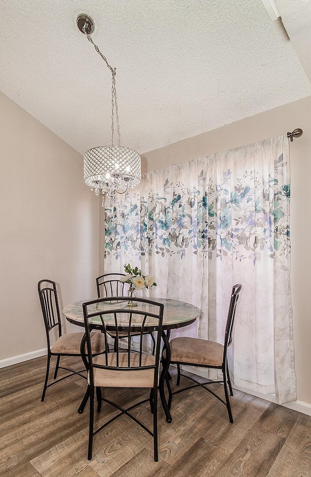 dining room featuring vaulted ceiling, hardwood / wood-style floors, a notable chandelier, and a textured ceiling