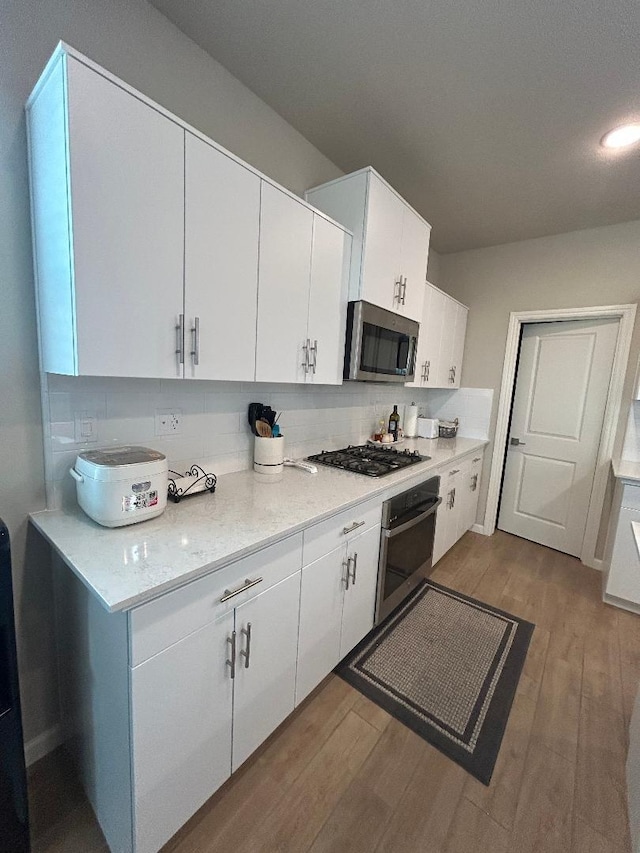 kitchen with white cabinetry, stainless steel appliances, light hardwood / wood-style floors, and backsplash