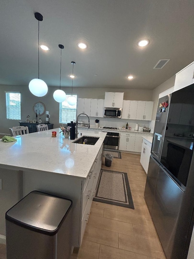 kitchen with sink, appliances with stainless steel finishes, hanging light fixtures, an island with sink, and white cabinets