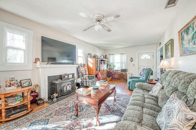 living room with a textured ceiling, light hardwood / wood-style flooring, ceiling fan, and a wood stove