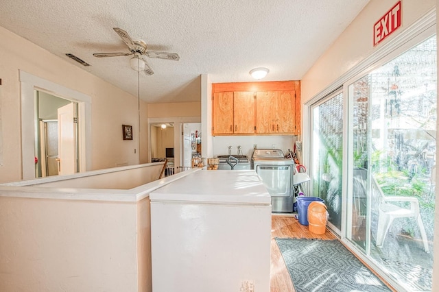 washroom with ceiling fan, separate washer and dryer, light hardwood / wood-style flooring, and a textured ceiling