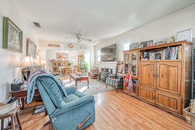 living room with ceiling fan, light hardwood / wood-style flooring, and a textured ceiling