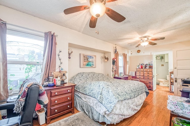 bedroom featuring ceiling fan, ensuite bathroom, a textured ceiling, and light wood-type flooring