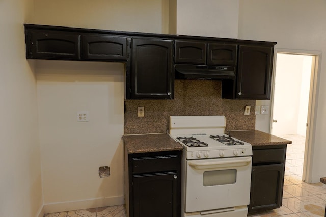 5140 E Belgravia Ave, Fresno, CA 93725 - kitchen featuring white gas range oven, under cabinet range hood, backsplash, dark countertops, and baseboards