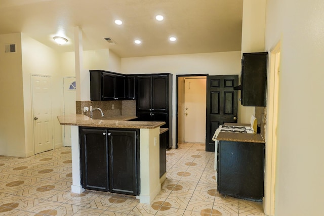 5140 E Belgravia Ave, Fresno, CA 93725 - kitchen with a peninsula, dark cabinets, recessed lighting, tasteful backsplash, and light tile patterned floors