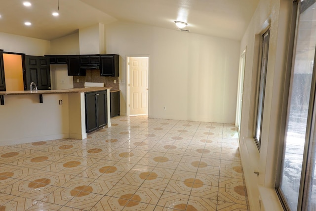 5140 E Belgravia Ave, Fresno, CA 93725 - kitchen with vaulted ceiling, decorative backsplash, light tile patterned floors, dark cabinetry, and light stone counters