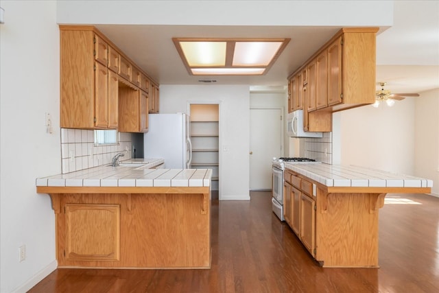 kitchen with dark hardwood / wood-style flooring, tile counters, white appliances, and kitchen peninsula