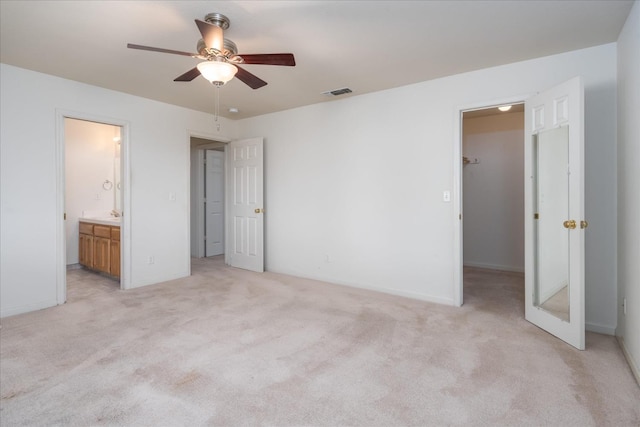 unfurnished bedroom featuring ceiling fan, ensuite bathroom, light carpet, a spacious closet, and a closet