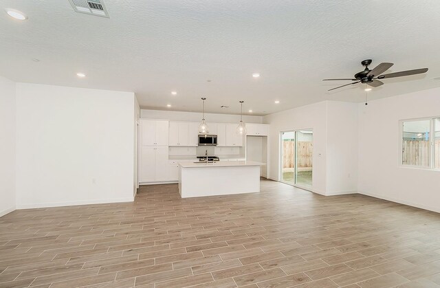 unfurnished living room with ceiling fan, light hardwood / wood-style floors, and a textured ceiling