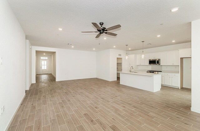 unfurnished living room with ceiling fan, sink, and a textured ceiling