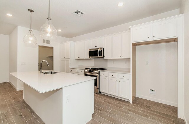 kitchen featuring stainless steel appliances, decorative light fixtures, an island with sink, and white cabinets