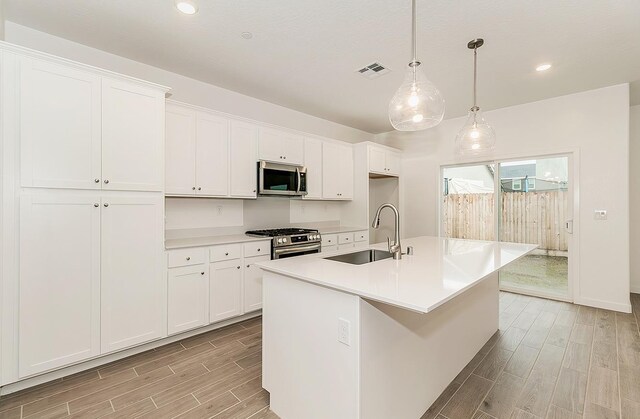 kitchen with hanging light fixtures, appliances with stainless steel finishes, sink, and a center island with sink