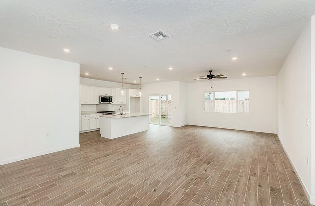 unfurnished living room featuring sink, light hardwood / wood-style flooring, and a textured ceiling