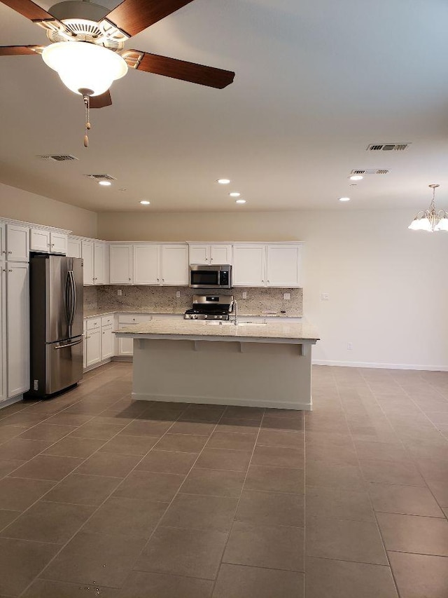 kitchen with a center island with sink, white cabinets, ceiling fan, stainless steel appliances, and backsplash