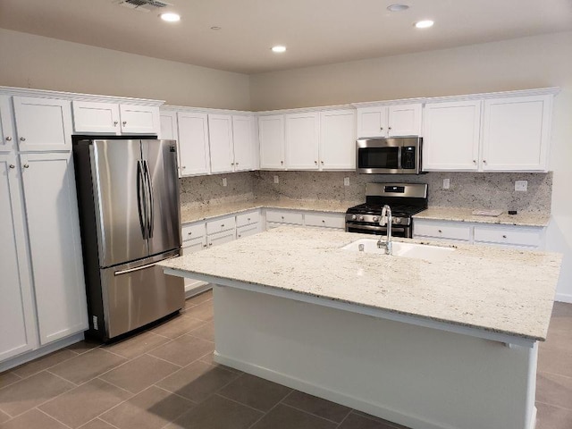 kitchen with light stone countertops, white cabinetry, appliances with stainless steel finishes, and a kitchen island with sink