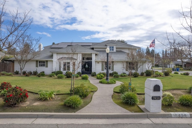 view of front of property with a front lawn and solar panels