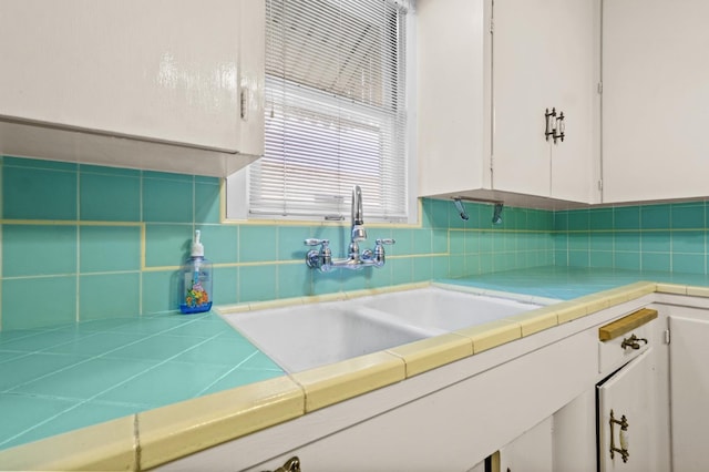 kitchen with tasteful backsplash, tile countertops, sink, and white cabinets