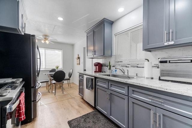 kitchen with gray cabinetry, decorative backsplash, light hardwood / wood-style floors, ceiling fan, and stainless steel appliances