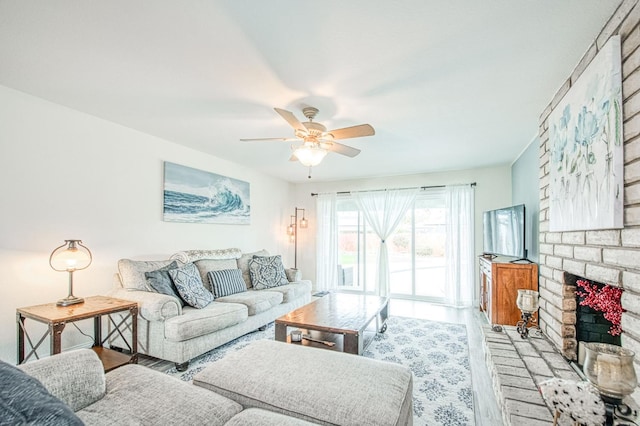 living room with a brick fireplace, ceiling fan, and light wood-type flooring