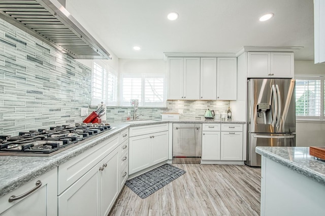 kitchen with appliances with stainless steel finishes, sink, white cabinets, light stone counters, and wall chimney range hood