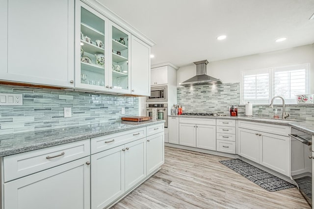 kitchen featuring light stone counters, appliances with stainless steel finishes, sink, and wall chimney range hood