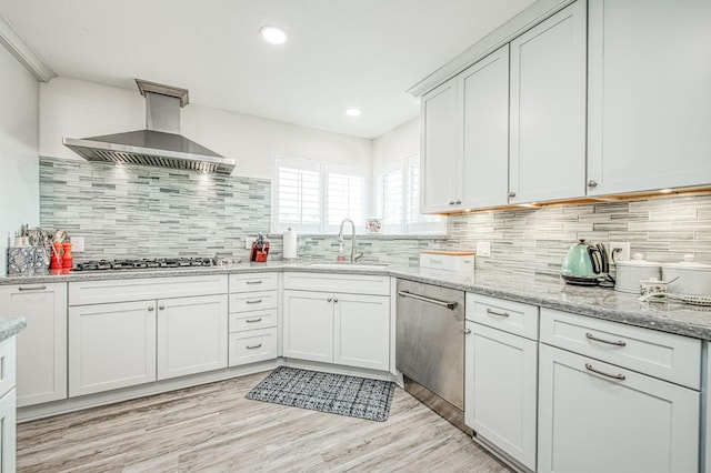 kitchen with sink, stainless steel appliances, light stone countertops, exhaust hood, and light wood-type flooring