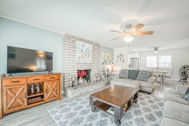 living room with a brick fireplace, ceiling fan, and light wood-type flooring