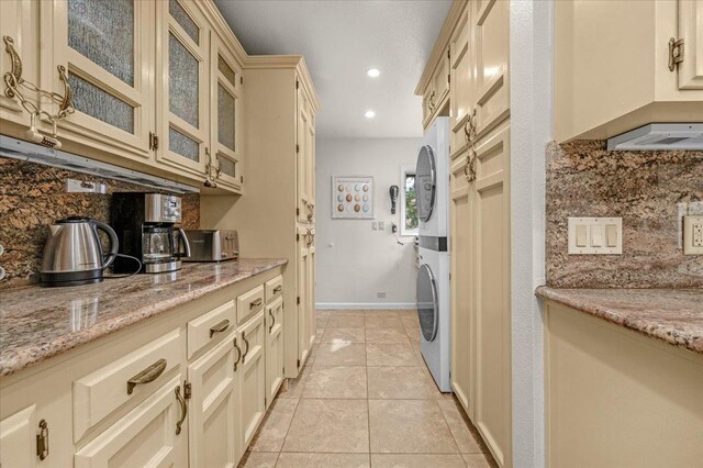 kitchen featuring tasteful backsplash, stacked washer / drying machine, light tile patterned floors, light stone counters, and cream cabinetry