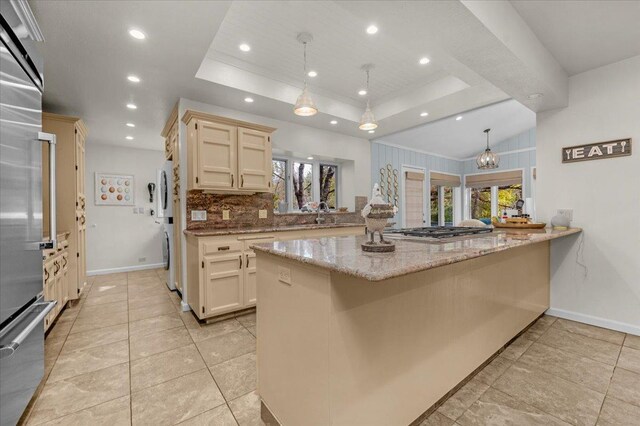 kitchen featuring light stone countertops, a tray ceiling, kitchen peninsula, and hanging light fixtures