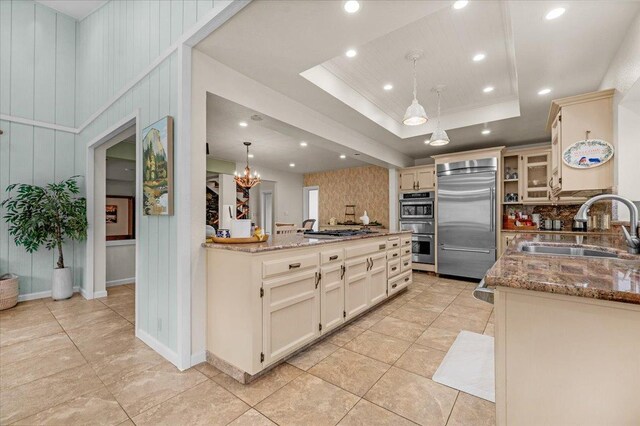 kitchen with decorative light fixtures, sink, light stone counters, a tray ceiling, and stainless steel appliances