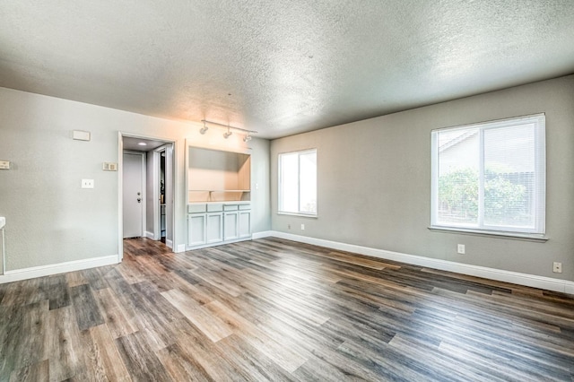 unfurnished room with track lighting, a textured ceiling, baseboards, and wood finished floors