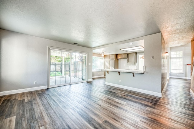 unfurnished living room featuring baseboards, plenty of natural light, dark wood-type flooring, and a textured ceiling