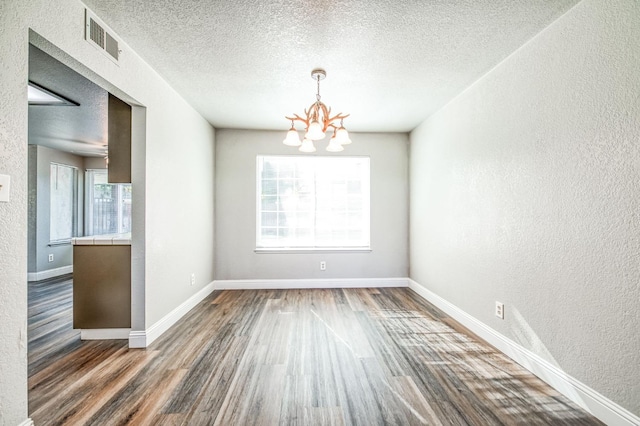 unfurnished dining area featuring an inviting chandelier, wood finished floors, visible vents, and a textured wall