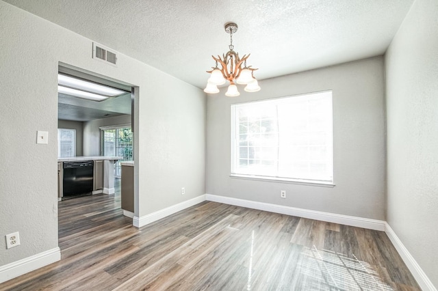 empty room featuring baseboards, wood finished floors, a textured wall, a notable chandelier, and a textured ceiling