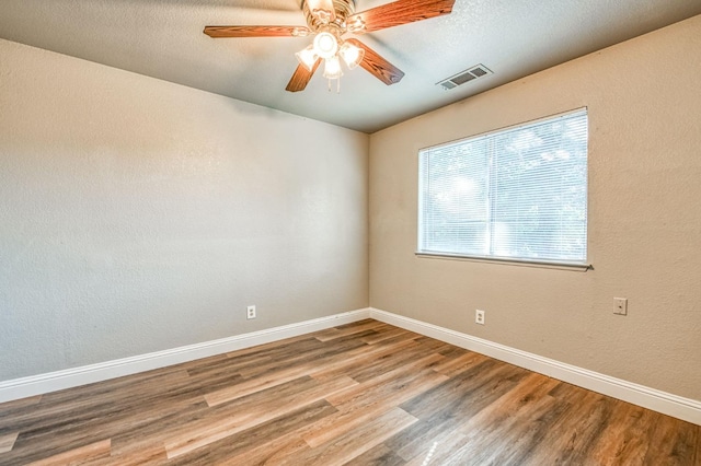 empty room with visible vents, a ceiling fan, a textured ceiling, wood finished floors, and baseboards