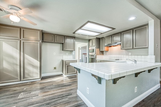 kitchen with dark wood-style floors, a peninsula, appliances with stainless steel finishes, and tile counters