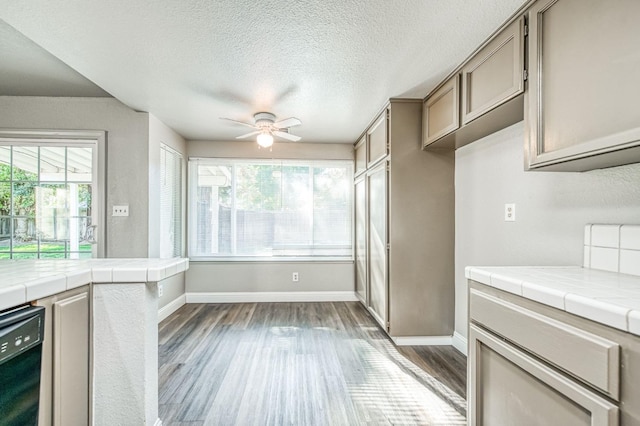 kitchen with dark wood finished floors, baseboards, black dishwasher, and tile counters