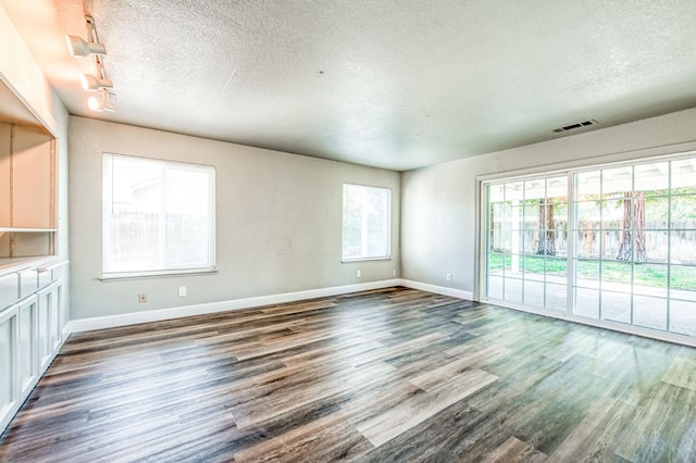 spare room featuring baseboards, wood finished floors, visible vents, and a textured ceiling