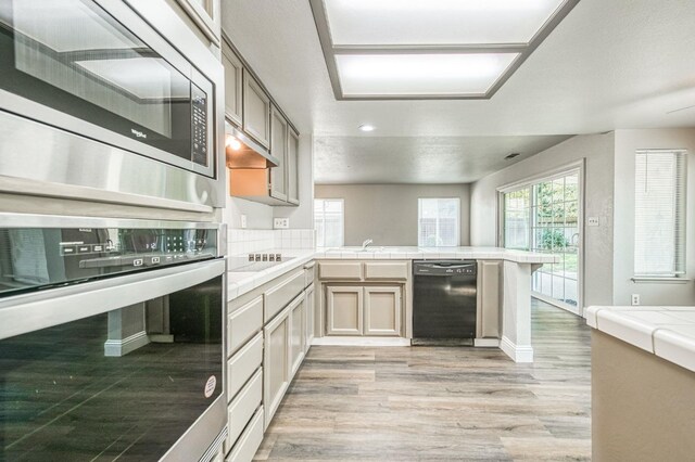 kitchen with tasteful backsplash, tile countertops, a peninsula, light wood-style floors, and black appliances