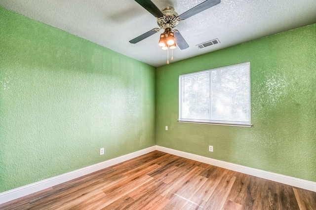 spare room featuring wood finished floors, visible vents, a textured wall, and baseboards