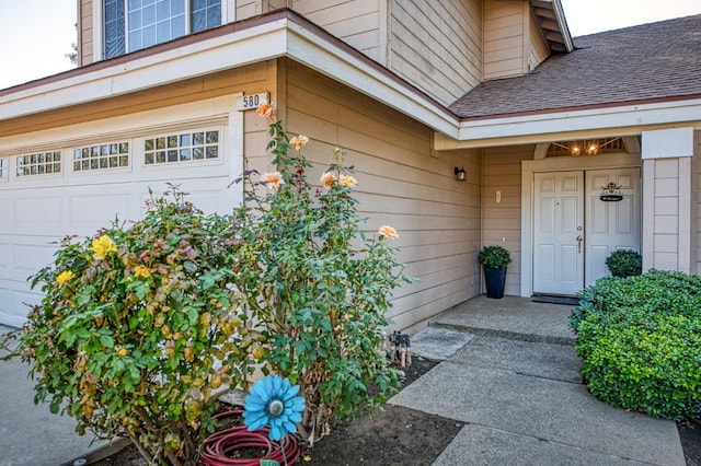 view of exterior entry with an attached garage and a shingled roof