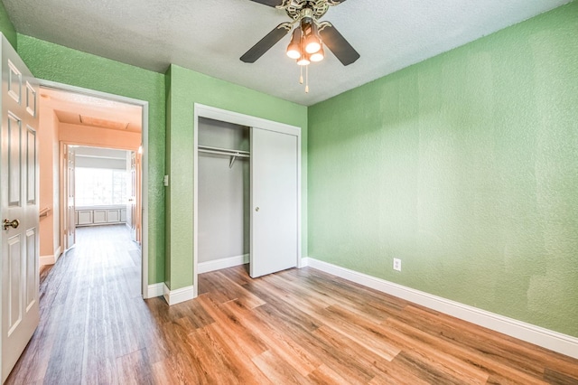 unfurnished bedroom featuring baseboards, light wood-style flooring, a textured wall, a closet, and a ceiling fan