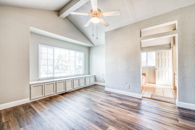 empty room featuring lofted ceiling with beams, plenty of natural light, wood finished floors, and baseboards