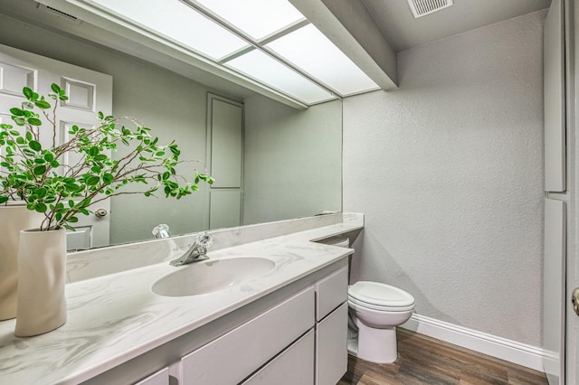 half bathroom with vanity, wood finished floors, baseboards, a skylight, and toilet